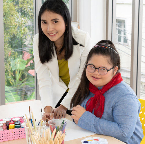 Portrait of happy teacher and girl with Down Syndrome in classroom