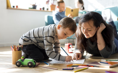 a kid writing on a piece of paper while being guided by an adult woman