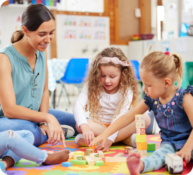 Female teacher and young children playing with building blocks