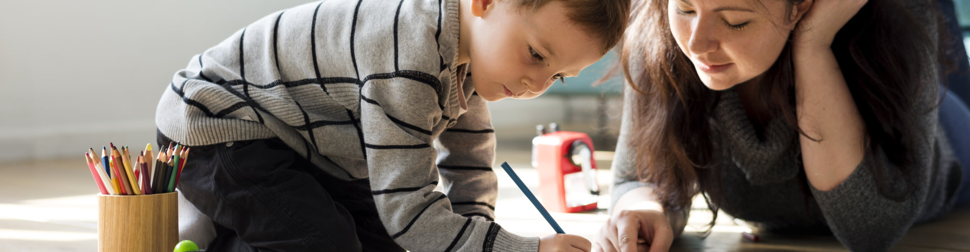 a kid writing on a piece of paper while being guided by an adult woman